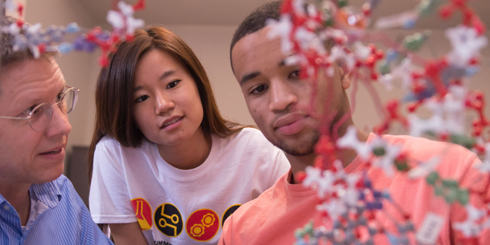 Close-up of students and professor examining molecule model.