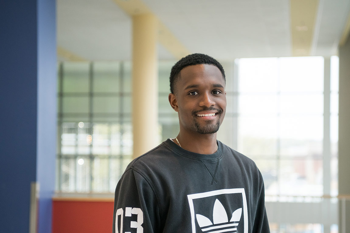 Jalen, looking friendly in front of the sunny windows inside the UMBC Commons building.